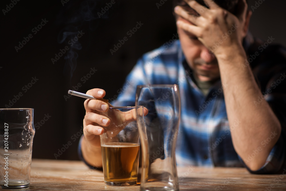 alcoholism, alcohol addiction and people concept - close up of male  alcoholic drinking beer and smoking cigarette at night Stock Photo