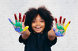 © twinsterphoto - African American playful and creative kid getting hands dirty with many colors - in white brick background.