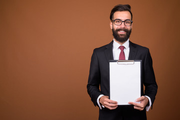 Young handsome bearded Persian businessman against brown backgro