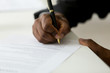 © fizkes - Close up of African American worker signing job contract, person being employed at new position, male client putting signature at document in office. Recruiting, promotion, legal documentation concept