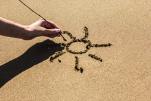 A Female Hand Draws The Sun On The Sand