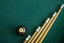 Eight black billiard ball on a green billiard table next to a group of a cue sticks