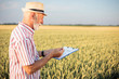 © Ivan - Senior farmer or agronomist examining wheat beads and filling out questionnaire while inspecting large organic farm. Healthy food production.
