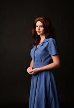 3/4 Portrait Of Brunette Lady Wearing Blue Dress. Posed On Black Studio Background.