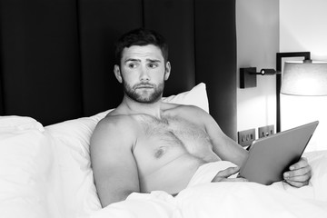 Wall Mural - Handsome,  naked male with beard using  ipad tablet in bed