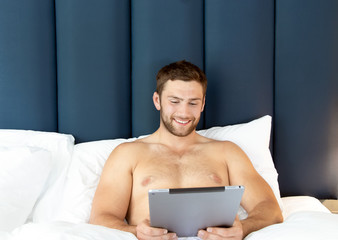 Wall Mural - Shirtless sexy hunky man with beard uses ipad tablet in bed