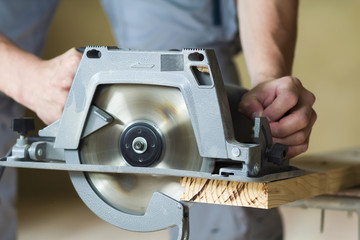 Close-up of muscular carpenter hands using new shiny modern powerful circular sharp electrical saw for cutting hard wooden board. Professional tools for construction and building concept.