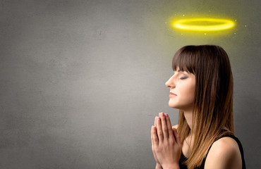 Young woman praying on a grey background with a shiny yellow halo above her head