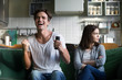 © fizkes - Angry girlfriend sulking while excited boyfriend football fan watching sport game holding remote control, annoyed wife disagreeing with husband about television channel choice sitting on sofa at home