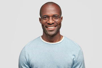 middle aged cheerful dark skinned male with shining smile, wears light blue sweater, round spectacle