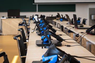 Close up of many virtual reality (VR) sets  in a classroom - headset, controller and computer. Gamer space, innovation or modern education concept.