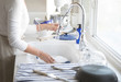 Photograph of a woman’s hands washing dishes in a white kitchen with blue accents 