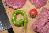 Fototapeta  - Beef steaks and ground beef, with red cherry tomato, green chili pepper and japanese knife on wooden cutting board.