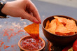 © golubovy - junk fast food and unhealthy eating. nacho tortilla chips in a bowl. woman hand dipping crunchy spicy triangular crisps in salsa tomato sauce