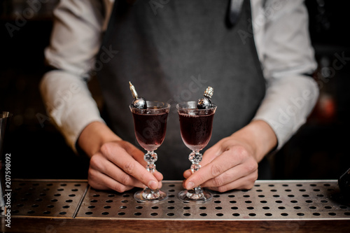 Fotografie, Obraz Bartender holding two elegant glasses filled with sweet summer Arnaud cocktail