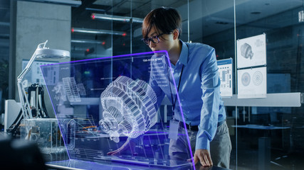 Asian Neural Network Engineer Uses Modern Computer With Transparent Holographic Display. Monitor Shows Visualization of a Mechanical Part. Shot in Modern Glass and Concrete Office.