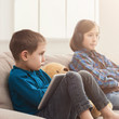 © Prostock-studio - Two kids with gadgets on couch at home