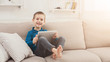 © Prostock-studio - Little boy using digital tablet on sofa at home