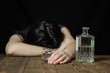 A drunk girl laid her head on a table, in her hand a glass of alcohol and a bottle, a wooden table, a black background