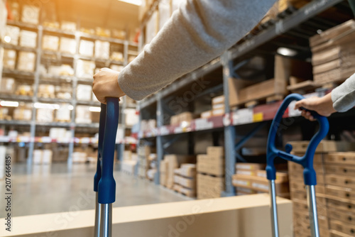 Fotomural Asian female worker pulling pallet truck or pushing a picking cart by two hands in storage warehouse with background of box on shelf structure