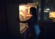 Sexy chubby woman craving and looking for food in a frige late at night. Girl dressed in homewear t-shirt and panties. Authentic atmosphere of the kitchen.