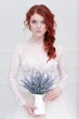 Tender retro portrait of a young beautiful dreamy redhead woman in beautiful white dress with bouquet of lavender.