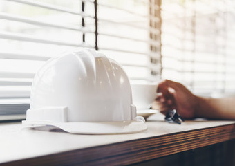 A white architect's helmet with a hand holding a coffee mug as the background blurred.