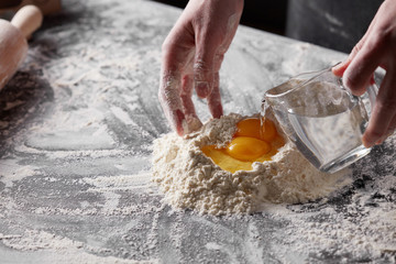 Wall Mural - women's hands pours water into the flour on the kitchen table. Preparation of dough for baking