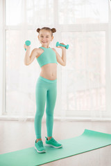 Wall Mural - Little sporty girl gymnast in sportswear doing exercises on a mat indoor