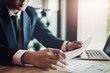 © Jirapong - contract concept , Business man reading agreement paper before sign document with use pen and laptop at work.