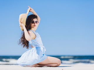 Wall Mural - Pretty girl sitting on a sandy beach by the blue sea.