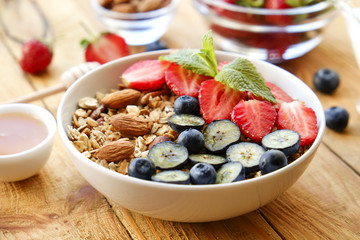 Wall Mural - Serving option of granola bowl with mix of nuts, cereals, fruits and berries, greek yogurt. Healthy vegetarian breakfast, organic strawberry, blueberry, mint, almond. Close up, top view, background.