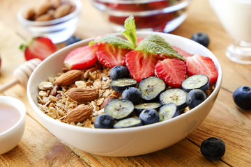 Wall Mural - Serving option of granola bowl with mix of nuts, cereals, fruits and berries, greek yogurt. Healthy vegetarian breakfast, organic strawberry, blueberry, mint, almond. Close up, top view, background.