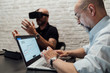 © Connect Images - Man using laptop, testing virtual reality headset