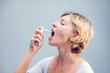 © Aleksej - Spray for sore throat. Photo of a woman who treats her throat with a spray and sprinkles it in her mouth. The concept of health and disease.