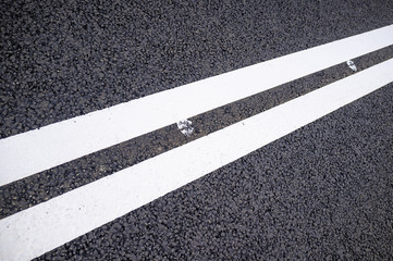 Two white solid lines on a new asphalt road. Close-up.