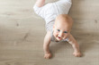 Cute little baby boy lying on hardwood and smiling. Child crawling over wooden parquet and looking up with happy face. View from above. Copyspace