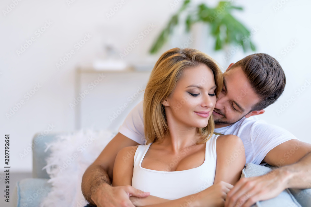 A beautiful young woman lying on the sofa with boyfriend hugging her ...