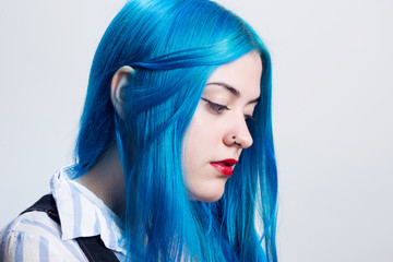 Portrait of a young woman with blue hair, indoors, in a white wall 