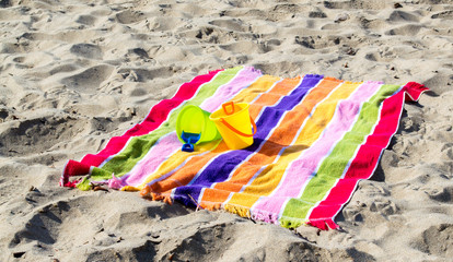 2 child's plastic sand pails and shovels with a colorful striped beach towel on a sandy beach 