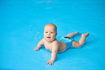 Happy, smiling little baby boy lying in blue swimming pool in water.