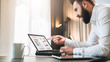 © foxyburrow - Young bearded businessman in white shirt is sitting at table in front of computer, showing pen on laptop screen with graphs, charts, diagrams. Online education, marketing. Business planning.