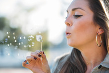 Portrait Of A Beautiful Young Woman Blowing Dandelion Flower. Freedom And Happiness Concept.