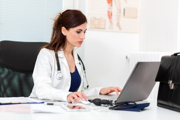 Beautiful female doctor in her studio typing on her laptop