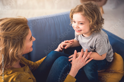 Fényképezés Mom and kid are grinning and looking into each-other eyes while staying down on sofa