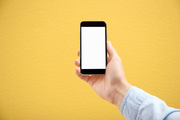 Young man holding mobile phone with blank screen in hand on color background