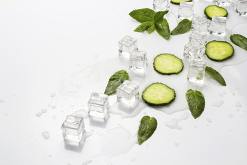 Spilled Glass with refreshing water, cucumber slices, mint leaves and ice cubes on a light background. Flat lay, top view