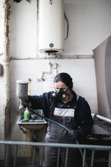 Wall Mural - Strong and worthy woman doing hard job. She using industrial spray compressor for painting some metal products.