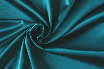 Close up of ripplesin shape of rose flower in aquamarine silk fabric. Satin textile background.