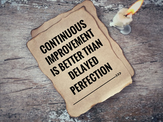 Wall Mural - Motivational and inspirational quote - ‘Continuous improvement is better than delayed perfection’ on a piece of paper. With blurred vintage styled background.